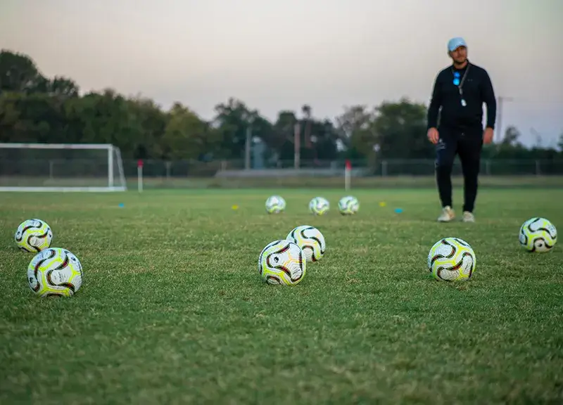 Coach walking next to soccer balls