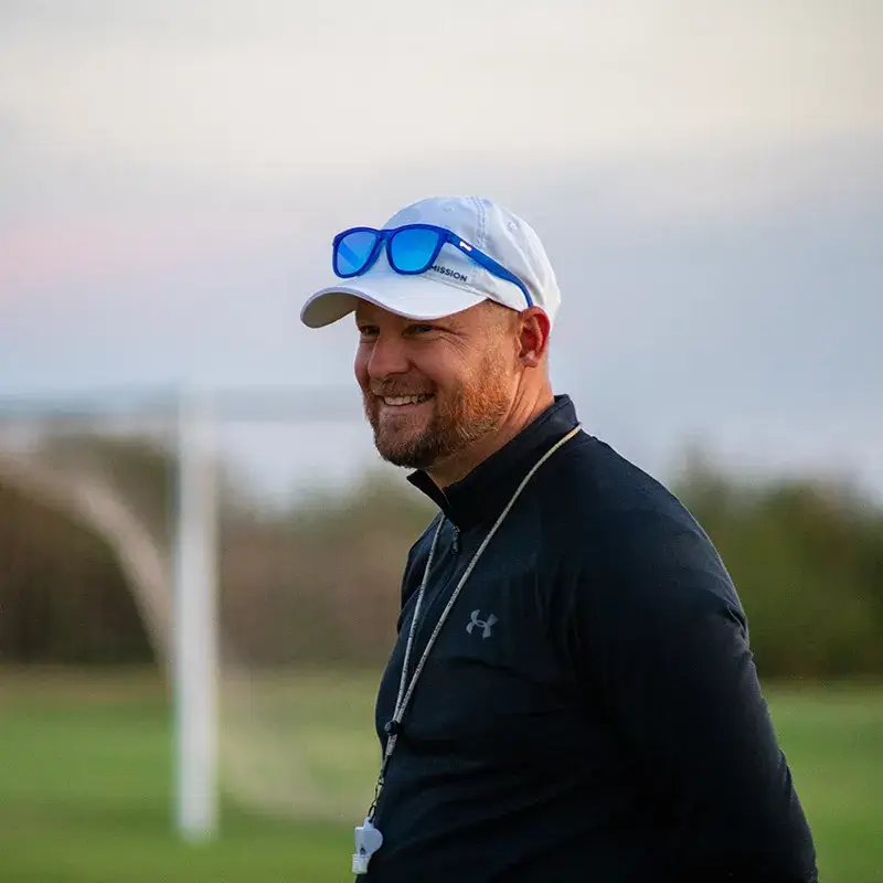 A soccer coach smiling while on the practice field
